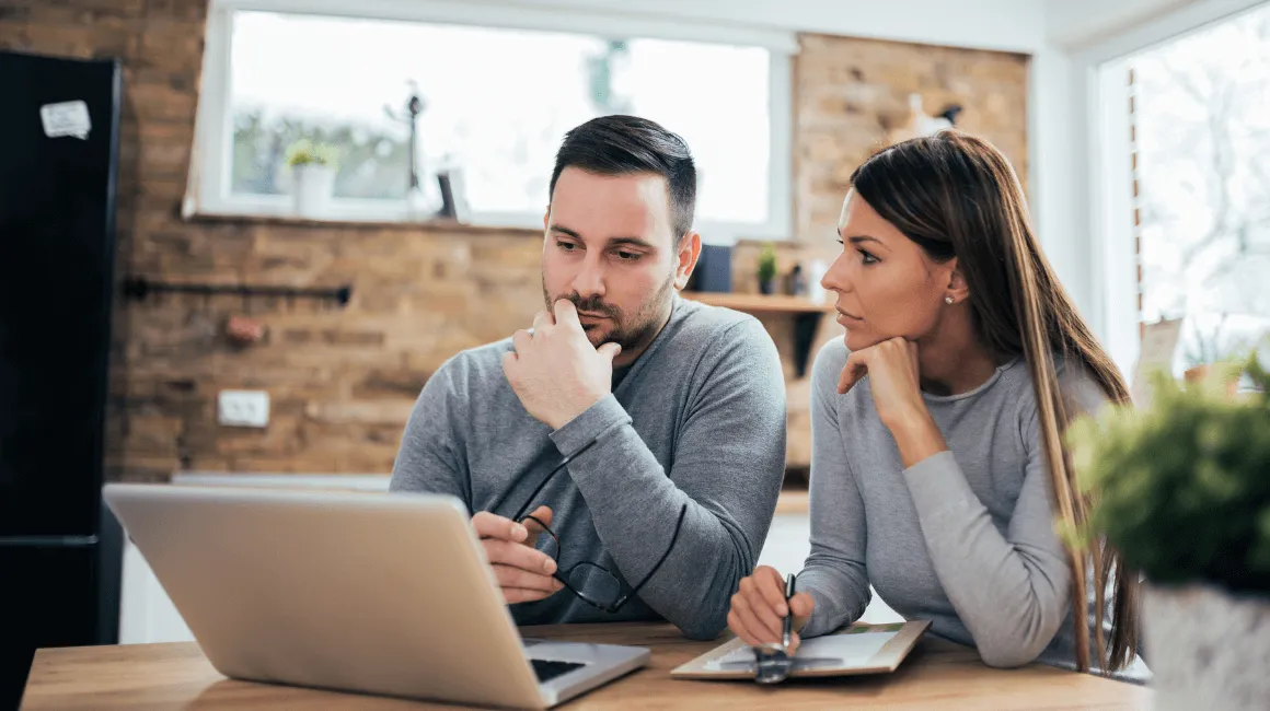 Para siedząca przy stole w domu, wspólnie analizująca dokumenty i informacje na laptopie.